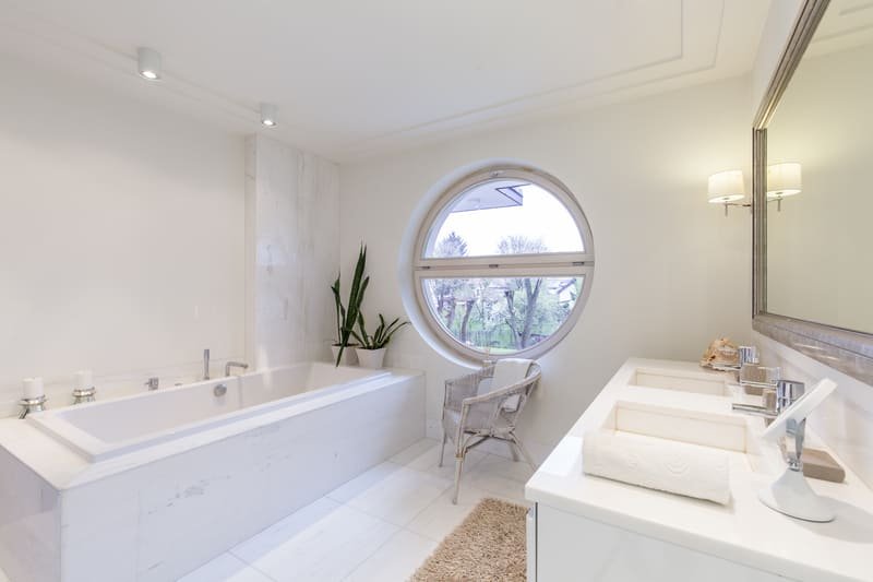 Cuarto de baño moderno y minimalista con bañera tipo jacuzzi, lavabo doble y ventana circular con vistas.
