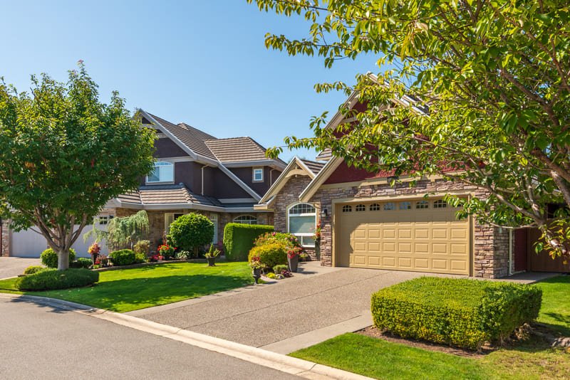 Casa de estilo rústico moderno con fachada de piedra, cochera doble y entrada de vehículos en vecindario residencial.